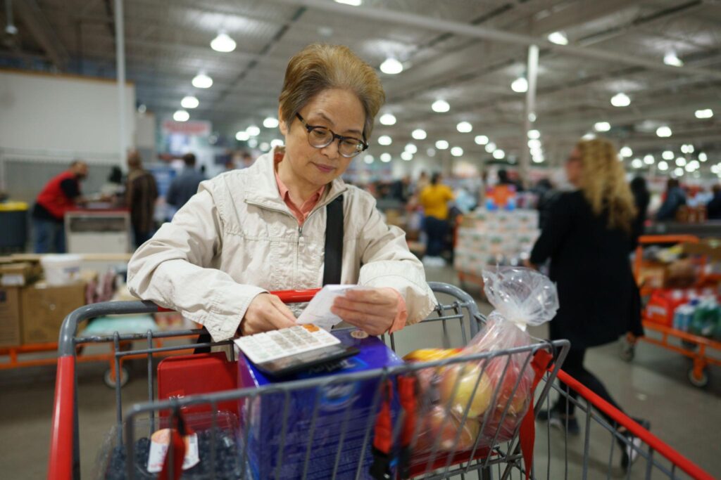Woman writing grocery list with calculator